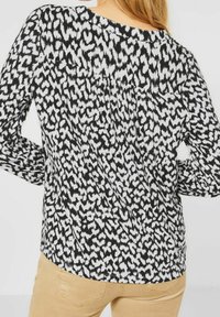 Černobílá dlouhá košile s abstraktním vzorem, volný střih a záhybové detaily podél zadního výstřihu.