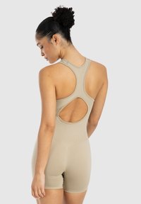 Body beige con un design aderente, texture a costine, stile racerback e un'apertura a chiave sul retro. Tessuto liscio, gambe corte.