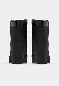 Botas pretas de plataforma com salto alto, acabamento mate e liso. Apresentam topo arredondado e salto grosso; incluem detalhes brilhantes e abas na parte traseira.