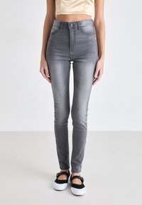 High-waisted gray denim jeans with a slim fit, subtle fading, and classic five-pocket design. Paired with black and white slip-on shoes.