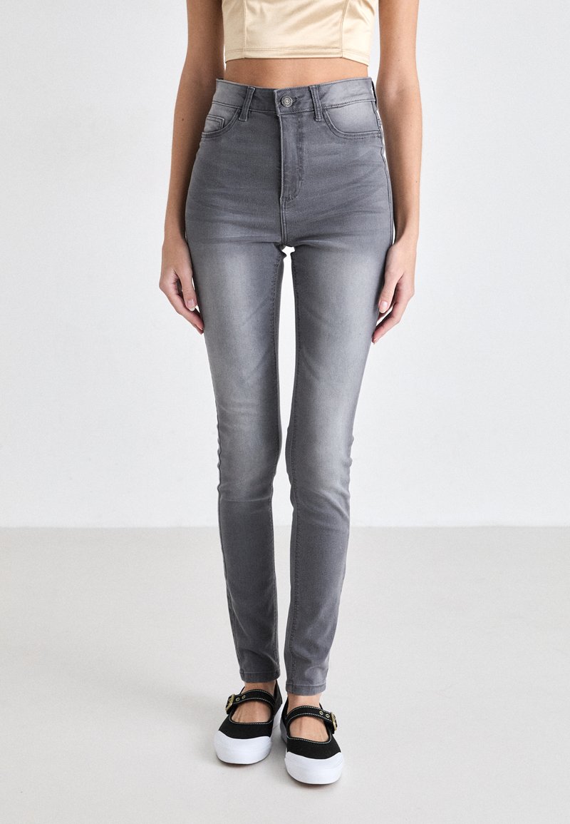 High-waisted gray denim jeans with a slim fit, subtle fading, and classic five-pocket design. Paired with black and white slip-on shoes.