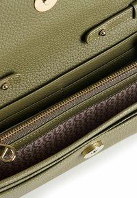 Interior de bolso de mano de cuero texturizado color verde oliva con un bolsillo con cremallera dorada y forro estampado. Cuenta con cierres magnéticos y de presión.