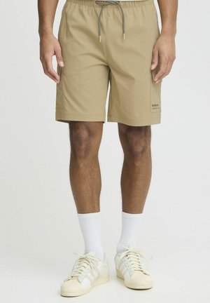 Beige zwemshorts met een elastische tailleband met trekkoord, zijkanten met zakken en een klein logo op het onderste been. Draag ze met witte sokken en sneakers.
