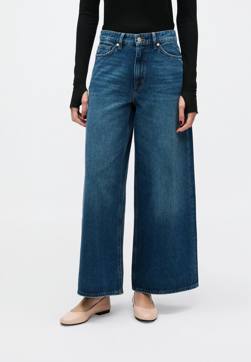 Παντελόνια παλατζόν από τζιν σε σκούρο μπλε, με ψηλή μέση, φαρδιά πόδια και κλασικό σχέδιο με πέντε τσέπες. Απαλό, υφασμένο ύφασμα.