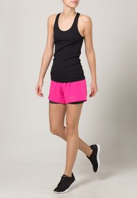 Musta hihaton urheilutoppi, yhdistetty kirkkaan pinkkeihin shortseihin, joissa on sisävuori. Mustat lenkkarit valkoisilla pohjilla täydentävät asun.