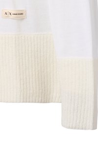 Weißer Strickpullover mit einem gerippten, cremefarbenen Saum. Enthält ein beiges Etikett mit schwarzer Schrift "A|X ARMANI EXCHANGE," das an der Seite angebracht ist.