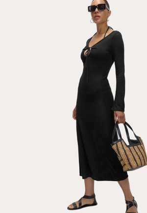 Zwarte lange jurk met een ronde hals en striksluiting, gecombineerd met een geweven tas en zwarte sandalen met bandjes. Glad textuur en aansluitend ontwerp.