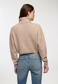 Przycięty, beżowy sweter z golfem w miękkim, teksturowanym splotem z prążkowanym kołnierzem, w parze z jasnoniebieskimi jeansami o wysokim stanie z tylnymi kieszeniami.