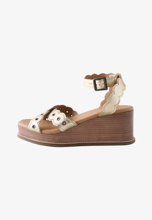 Sandalia cuña de cuero beige con bordes festoneados, ojales metálicos, correa en el tobillo y suela plataforma de madera.