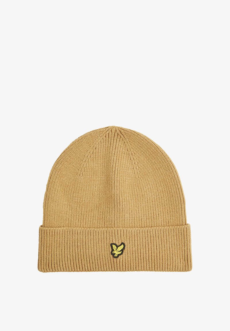 Knit beanie in tan with a ribbed texture. Features a folded cuff and a small black and yellow logo on the front.