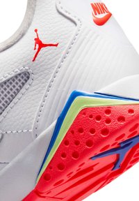 Λευκό αθλητικό παπούτσι Nike Air Jordan με υφή κόκκινης σόλας, κόκκινα λογότυπα Jumpman και Nike, με μπλε και πράσινες λεπτομέρειες κοντά στη φτέρνα.