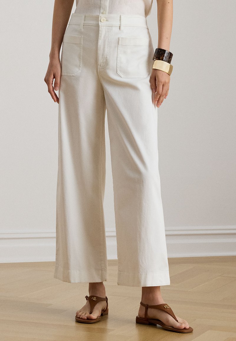 Φαρδιά βαμβακερή παντελόνα σε κρεμ χρώμα με ομαλή υφή, που διαθέτει τσέπες μπροστά και πίσω και σχεδιασμό με ψηλή μέση.