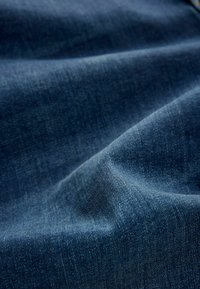 Tissu en denim bleu foncé avec une texture lisse, présentant de subtiles variations d'ombre et un léger motif de tissage diagonal.