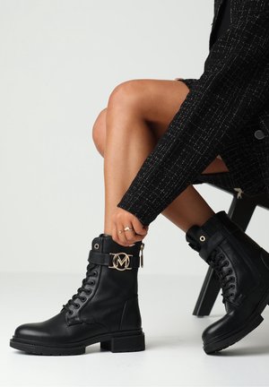 Botas de tornozelo de cuero negro con un acabado texturizado, puntera redonda, parte delantera con cordones, detalles en hardware dorado y una correa decorativa con un logotipo.