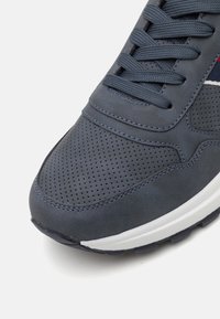 Baskets bleu marine avec une tige perforée et une texture en daim lisse. Caractéristiques d'une semelle intermédiaire blanche et de coutures contrastées le long des bords.