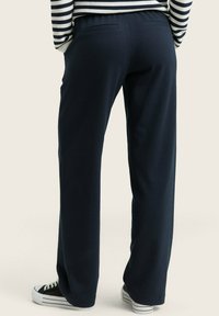 Pantalons larges bleu marine en tissu texturé avec une taille élastique et deux poches arrière. Associés à des baskets noir et blanc.