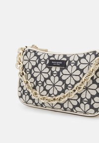Borsa a mano in stoffa bianca e nera con motivo floreale, dotata di tracolla a catena dorata, chiusura con zip e patch con il logo Kate Spade.