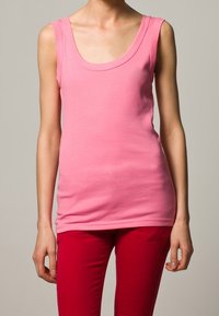 Roze mouwloos topje met een ronde hals, gemaakt van gladde stof; gedragen met strakke rode broeken. Eenvoudig ontwerp, zonder patronen of accenten.