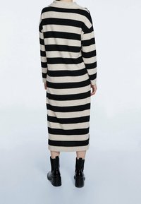 Vestito a strisce con ampie strisce orizzontali nere e beige, maniche lunghe, colletto e taglio a metà gamba. Indossato con stivaletti neri chunky alla caviglia.