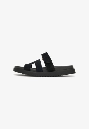 Czarna zamszowa sandałka z dwoma szerokimi paskami, regulowanym zapięciem na rzep oraz teksturowaną czarną gumową podeszwą o niskim profilu.