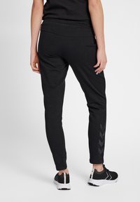 Svarta joggers i ankellängd med slät textur, elastisk midja och fiskbensmönsterdetalj på underbenet. Stylistiskt med svarta träningsskor.