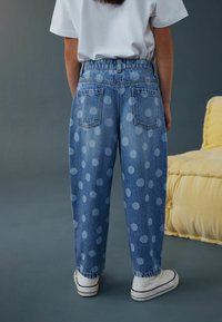 Blugi din denim cu croială lejeră, având un model cu buline albastre deschise, talie înaltă și buzunare pe spate. Purtate cu adidași albi.
