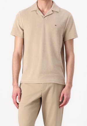 Beige short-sleeve polo shirt made of soft fabric with a collar and a small logo on the left chest, paired with light beige pants.