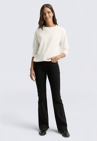 White sweater with a round neckline and three-quarter sleeves paired with black flared jeans. The outfit features a relaxed fit and smooth texture.
