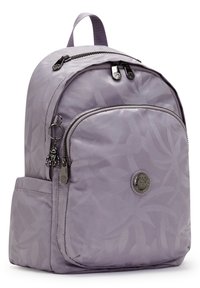 Mochila de tela morada con un patrón de hojas, dos compartimentos con cremallera, un logo circular y un pequeño charm adherido a la cremallera.