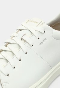 Λευκό δερμάτινο αθλητικό παπούτσι με επίπεδα κορδόνια, ανάγλυφο λογότυπο "GEOX", μινιμαλιστικό σχεδιασμό, λεία υφή και λαστιχένια εξωτερική σόλα.