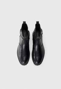 Botines de cuero negro que presentan una superficie lisa, puntera redondeada, cremallera lateral y detalles cosidos a lo largo de la suela.