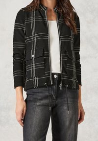 Black zip-up jacket with white plaid pattern, two front patch pockets, textured fabric, and adjustable drawstring at the hem.