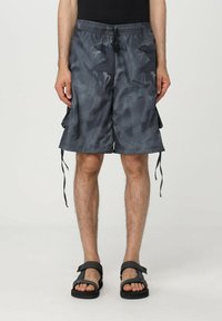 Pantaloni corti grigi di lunghezza media realizzati in un tessuto leggero con un motivo sottile, caratterizzati da una vita con cordoncino e tasche laterali. Sono indossate delle ciabatte piatte.