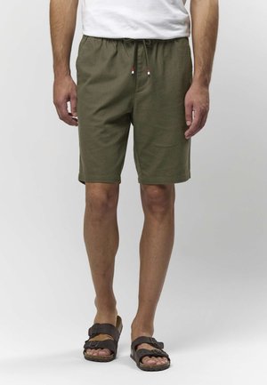 Olivově zelené šortky s elastickým pasem a šňůrkou, s jemnou texturou. Kombinované s tmavě hnědými sandály.