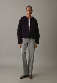 Giacca trapuntata viola con scollo rotondo, maniche lunghe e vestibilità corta; abbinata a pantaloni grigi chiari con una leggera scintilla.