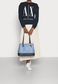 Ljusblå handväska med marinblå detaljer och silverbeslag, kombinerad med en marinblå sweatshirt med en vit logga och en veckad cremefärgad kjol.