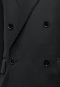 Detailný záber na čierny dvojradový blejzer so štyrmi čiernymi gombíkmi a dvoma vreckami s klopou.