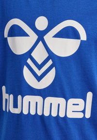 Hvid stiliseret humlebi-logo og "hummel" tekst trykt på en blå stofbaggrund.
