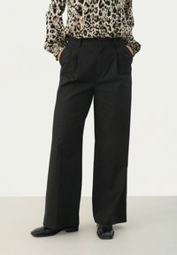 Black wide-leg trousers with pleats, made from smooth fabric. Worn with a patterned top, featuring a high waist and side pockets.