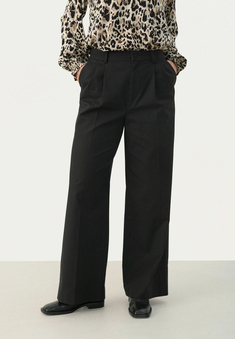 Black wide-leg trousers with pleats, made from smooth fabric. Worn with a patterned top, featuring a high waist and side pockets.
