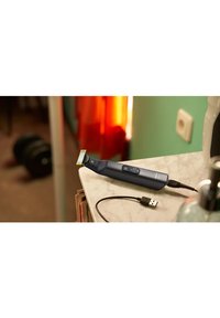 Oplaadbare trimmer met een donkerblauwe behuizing, gele trimkop, digitale display en een zwarte USB-oplaadkabel op een marmeren oppervlak.