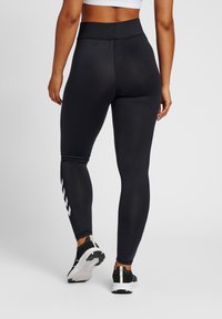 Høytlivs svarte leggings med en glatt tekstur, som har hvite chevron-mønstre langs de nedre bena og en tettsittende design.