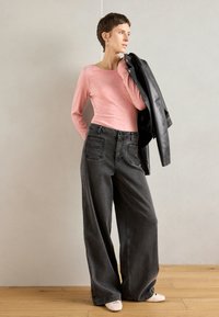 Svetloružový top s dlhým rukávom skombinovaný s vysokými pásmi a širokými šedými džínsami. Model drží čiernu koženú bundu. Jednoduchý dizajn a mäkké textúry.