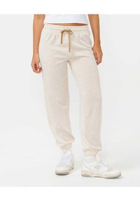 Ljusbeige joggerbyxor med dragsko i midjan, elastiska muddar och en mjuk textur, kombinerat med vita sneakers.