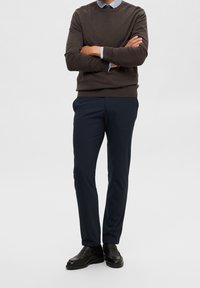 Brun stickad tröja, marinblå byxor, svarta loafers; tröjan har en rund halsringning och ribbade manschetter; byxorna är skräddarsydda med sidofickor.