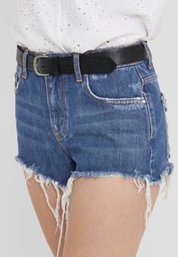 Pantalones cortos de mezclilla en azul oscuro con dobladillo deshilachado, que cuentan con dos bolsillos frontales y un cinturón de piel negro con una hebilla plateada. Diseño casual.