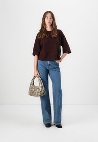 Brun kortermet genser, blå vide jeans og en liten håndveske med slangerprint. Modellen står mot en hvit bakgrunn.