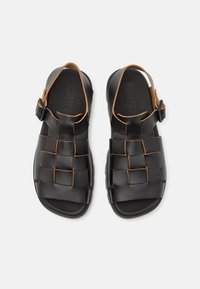 Sandali in pelle nera con un design intrecciato, dettagli marroni, una cintura regolabile e una soletta texture con il logo del marchio.