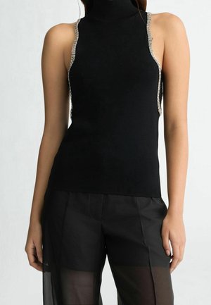 Haut sans manches à col roulé noir avec bordure en strass le long des emmanchures, associé à un pantalon large noir transparent.