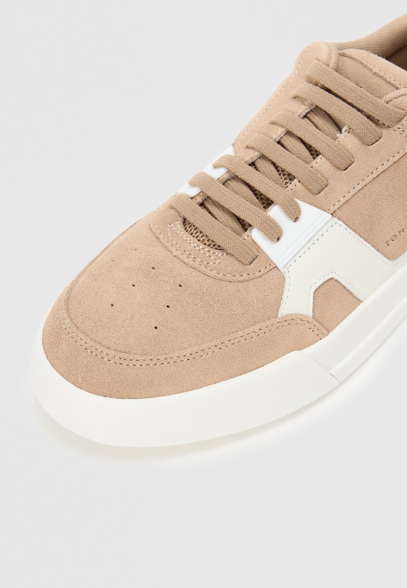 Baskets en daim marron clair avec des accents blancs, présentant un orteil perforé, des lacets plats et une semelle en caoutchouc texturée pour une meilleure adhérence.